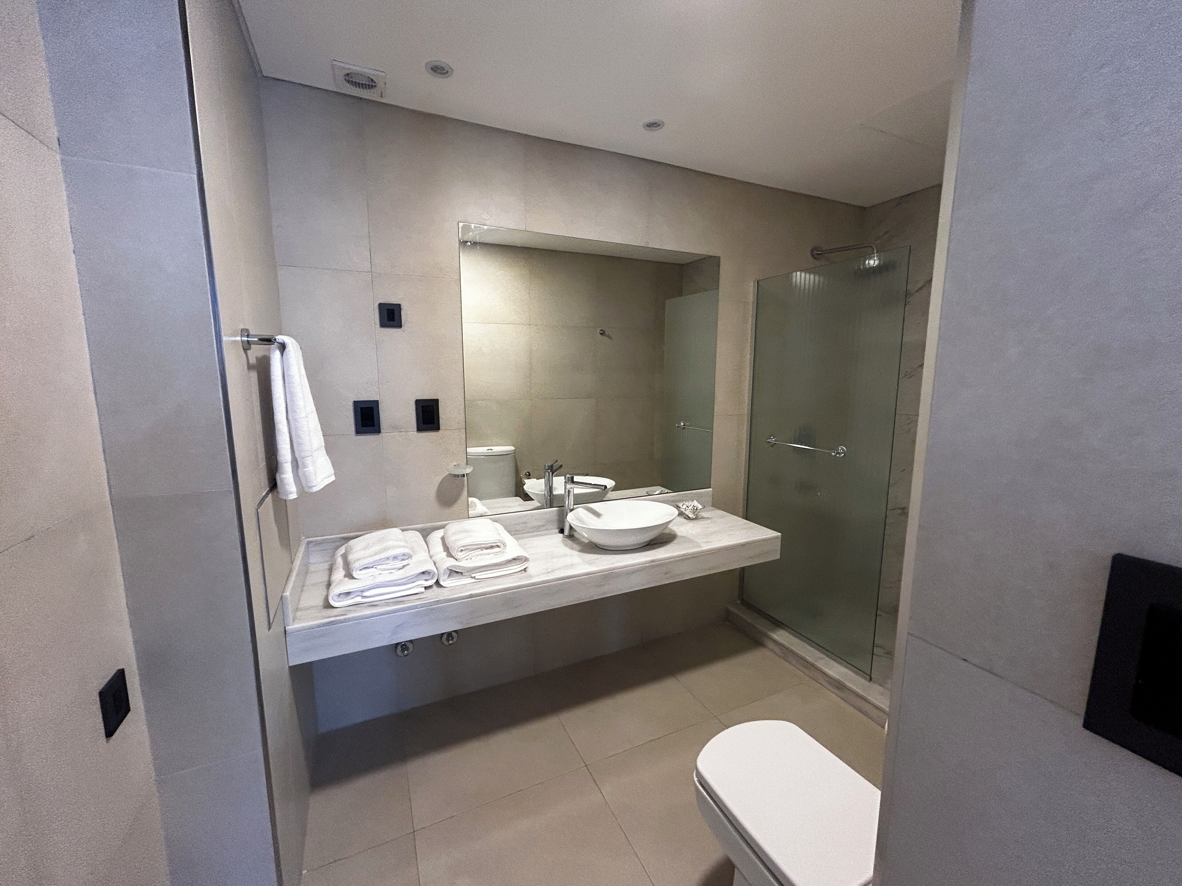 Une salle de bain moderne avec un grand miroir, un lavabo sur colonne, des toilettes et une douche à parois de verre.