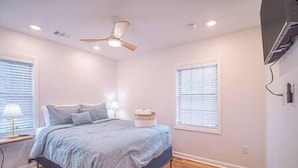 Een slaapkamer met een bed, een plafondventilator en een raam met jaloezieën.