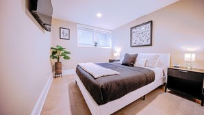 A bedroom with a large bed, a bedside table, a lamp, and a potted plant. - The Grand Slam - The Battery ATL (Smyrna)