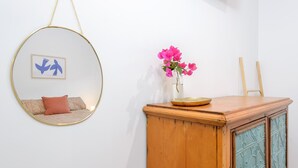 Una habitación con un espejo circular colgante, un mueble de madera con puerta de cristal y un jarrón con flores rosas encima.