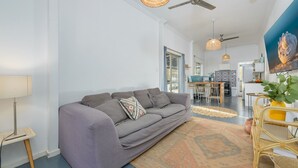 Una sala de estar moderna con un sofá gris, una lámpara de pie tejida y un comedor con cocina al fondo.