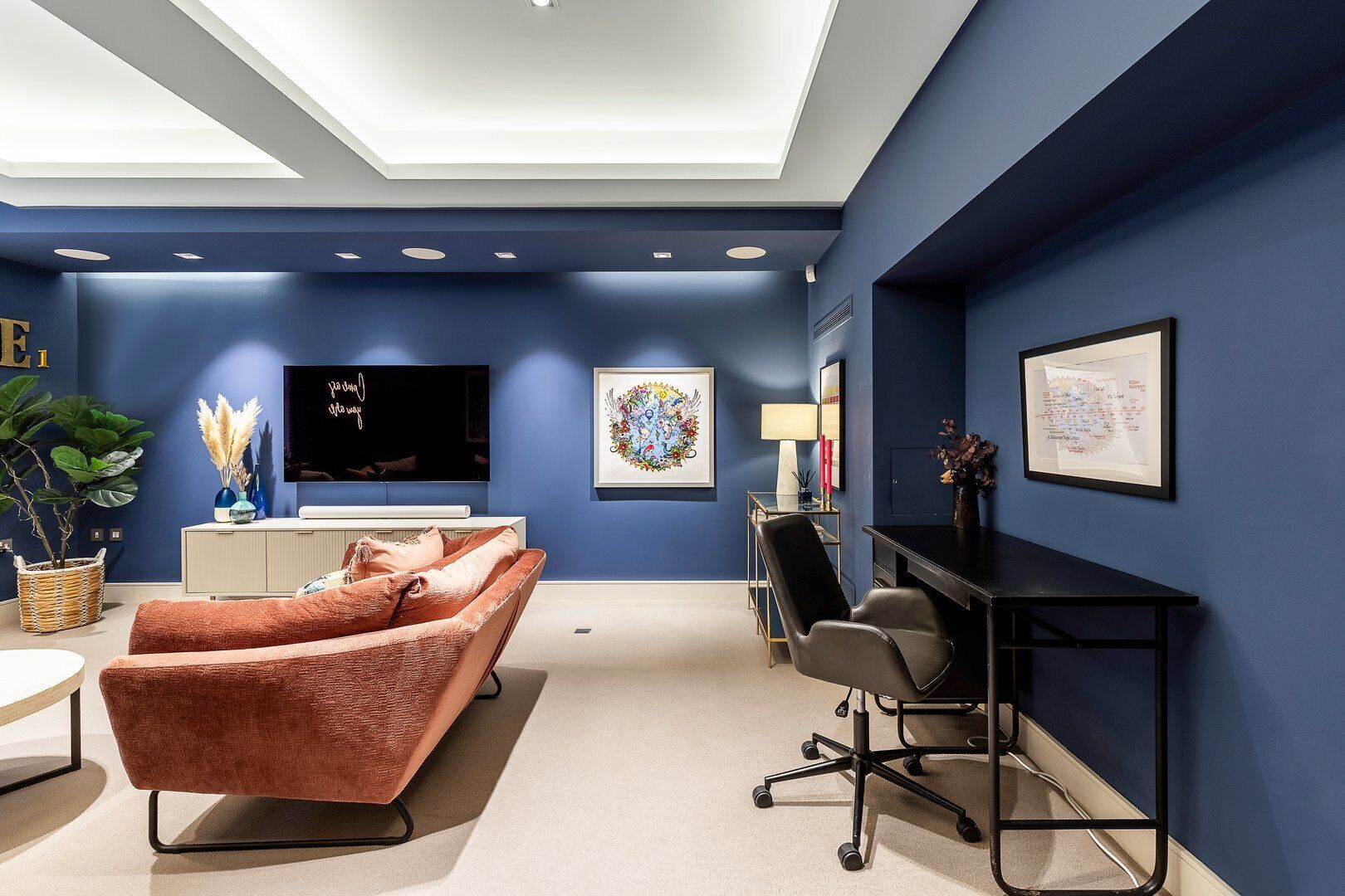 Une chambre moderne avec un mur d’accent bleu, un coin salon confortable avec un canapé et des fauteuils, un bureau avec un ordinateur et un téléviseur à écran plat fixé au mur.