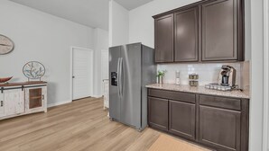 A modern kitchen with dark cabinets, a stainless steel refrigerator, and a wooden floor.
