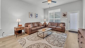 A living room with a brown leather sofa, two side tables with lamps, a coffee table, patterned rug, ceiling fan, and a door with a window.