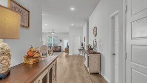 A spacious hallway with wooden flooring, a wooden console table with decorative items, a white door, and a ceiling fan.