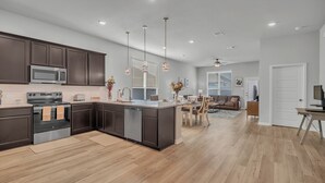 A modern kitchen with dark cabinetry, a central island, and a dining area with a sofa and table.