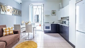 A modern kitchen with white cabinets, a microwave, and a stove. There is a dining area with a table and chairs, and a living room with a sofa and a rug. - Bilocale in zona Isola - Garibaldi (Milan)