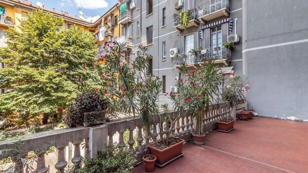 A courtyard with potted plants, a stone balustrade, and multi-story buildings with balconies. - Bilocale in zona Isola - Garibaldi (Milan)