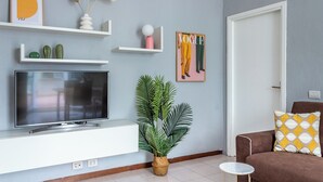 A living room with a flat-screen TV, a potted plant, a sofa with patterned cushions, and a framed picture on the wall. - Bilocale in zona Isola - Garibaldi (Milan)