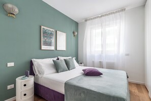 Une chambre à coucher avec un lit, une table de chevet, une lampe fixée au mur et deux tableaux encadrés.