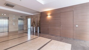 En modern entréhall med hissar, en receptionsdisk och en stor väggpanel i trä.