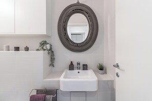 Une salle de bain avec un lavabo blanc, un miroir rond et une plante en pot.