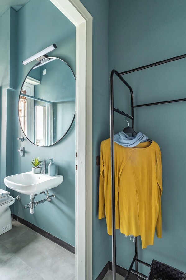 A bathroom with a white sink, a round mirror, and a towel rack with a yellow towel.