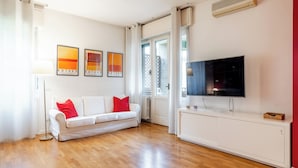 A modern living room with a white sofa, red cushions, a flat-screen TV, and artwork on the wall. - [Niguarda] Bright and comfortable Flat (Milan)