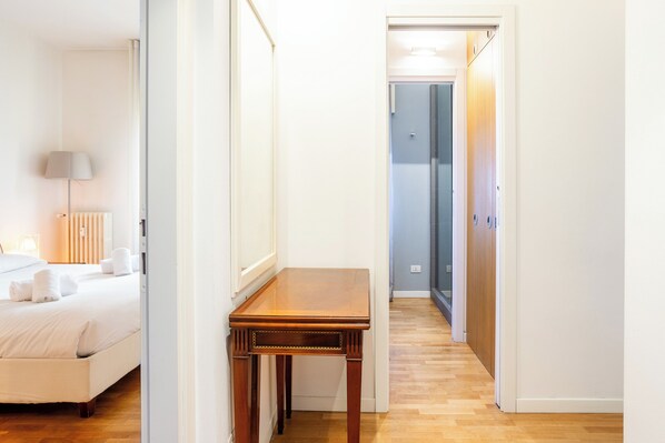 A hotel room with a bed, bedside table, and a hallway leading to a bathroom.