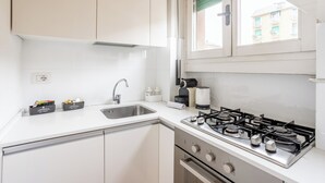 A kitchen with white cabinets, a stainless steel sink, a gas stove, and a window with a view of buildings. - [Niguarda] Bright and comfortable Flat (Milan)