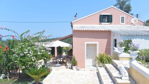 A pink house with a tiled patio, a dining area, and potted plants. - Villa Eleni Peritheia by Corfu Escapes (Corfu)