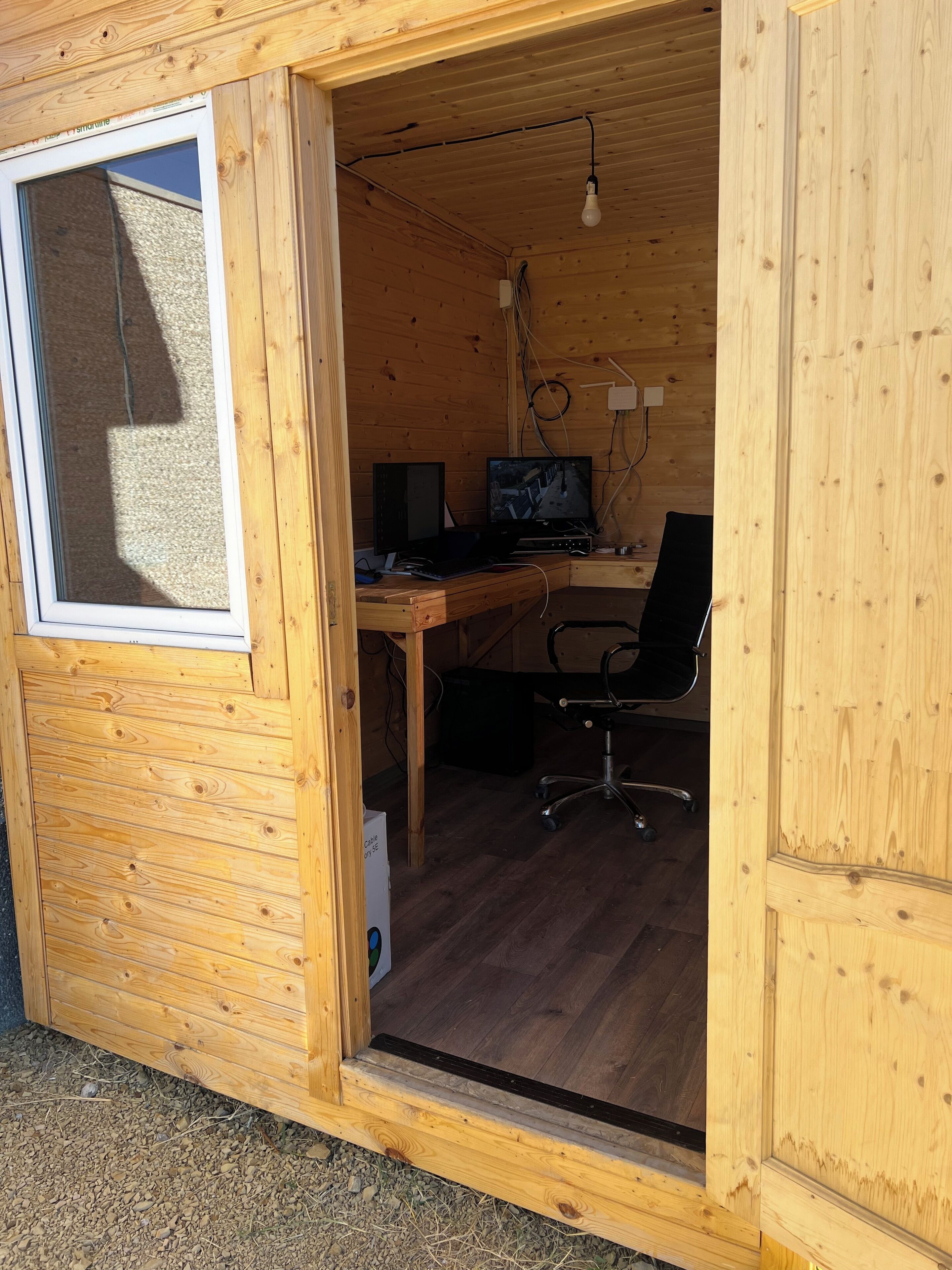 A wooden cabin with a desk, two monitors, and a chair.