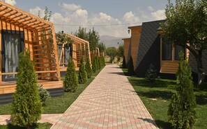 A pathway leading to wooden cabins with a clear sky and mountains in the background. - Hidden Garden Resort (Garni)