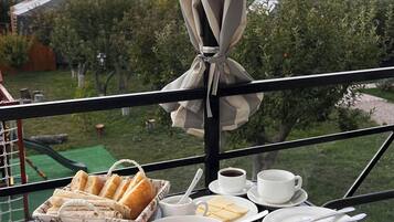 A table set with breakfast items including bread, sausages, and pastries, with a view of trees and a clear sky.