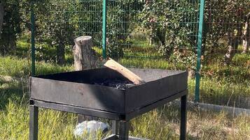 A metal table with a fire pit in the center, surrounded by grass and a fence.