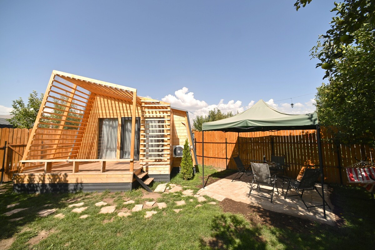 A wooden cabin with a sloped roof, a small deck, and a covered patio area with outdoor furniture.