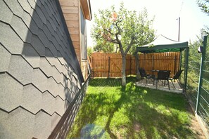 A backyard with a wooden fence, a tree, and a patio area with chairs and a table. - Hidden Garden Resort (Garni)