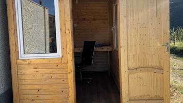Una piccola baita di legno con una sola porta aperta, da cui si intravede una scrivania e una sedia all'interno.