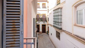 A narrow alleyway between buildings with a metal gate, a door with a window, and a balcony with railings. - Malhara Apartment (Sevilla)