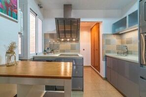 A modern kitchen with a central island, stainless steel appliances, and a view into the adjacent dining area. - Malhara Apartment (Sevilla)