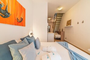 Una camera da letto con un letto, cuscini, un quadro, una scala e una piccola scrivania.