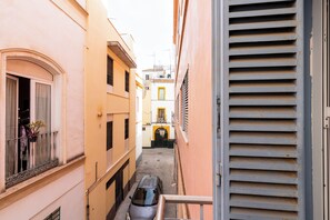 A narrow alleyway with buildings on either side, a parked car, and a visible door on the right. - Malhara Apartment (Sevilla)