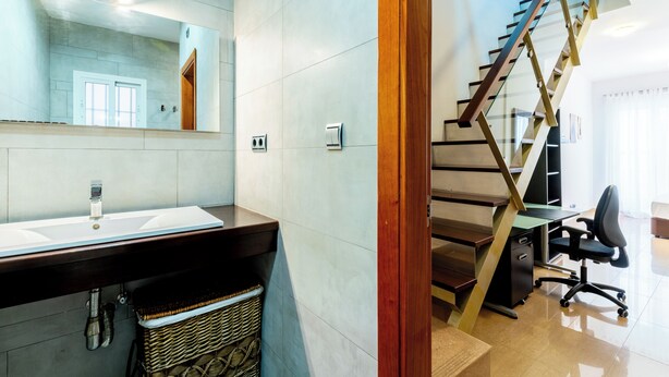 A modern bathroom with a large mirror, a sink, and a staircase leading to another level. - Malhara Apartment (Sevilla)