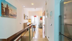 A modern kitchen with a stainless steel refrigerator, a dining area with a table and chairs, and a hallway with a staircase. - Malhara Apartment (Sevilla)
