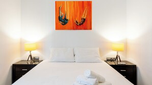 A hotel room with a bed, two bedside tables with lamps, and a painting on the wall. - Malhara Apartment (Sevilla)