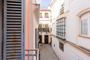 A narrow alleyway between buildings with a metal gate, a door with a window, and a balcony with railings. - Malhara Apartment (Sevilla)
