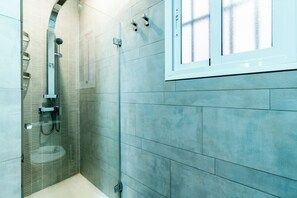 A modern bathroom with a glass-enclosed shower, tiled walls, and a window. - Malhara Apartment (Sevilla)