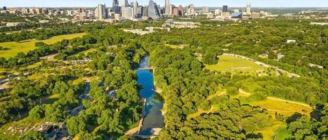 An aerial view of a city with a river, green parks, and a skyline of modern buildings.
