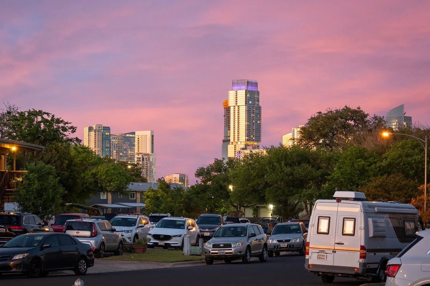 A parking lot with various vehicles, including cars and a van, and a tall building in the background.