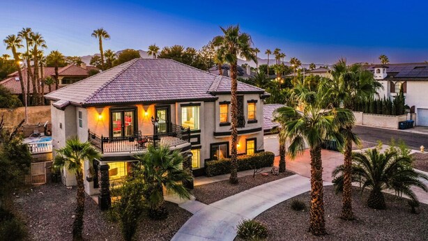 A two-story house with a balcony, surrounded by palm trees and a clear sky.