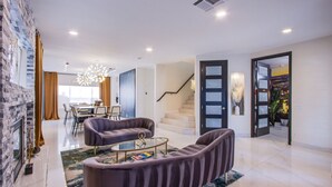 A modern living room with a fireplace, a staircase, and a dining area.