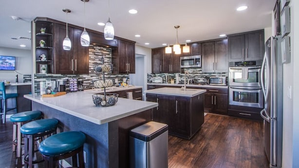 A modern kitchen with dark wood cabinets, stainless steel appliances, and a central island with bar stools. - The Oasis, a Vegas Villa (Las Vegas)