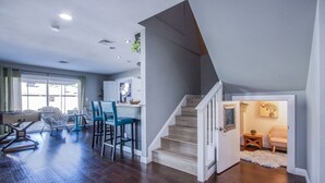 A spacious living area with a kitchen, a dining area with blue chairs, and a staircase leading to a second floor. - The Oasis, a Vegas Villa (Las Vegas)