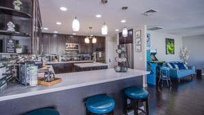 A modern kitchen with a central island, bar stools, and a seating area with a blue sofa. - The Oasis, a Vegas Villa (Las Vegas)
