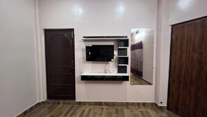 A room with a wooden floor, a TV mounted on the wall, and a wardrobe. - 100m from Ganges River & Dasashwamedh Ghat, 1-bedroom  in Varanasi with AC, WiFi (Varanasi)