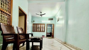 A hallway with two wooden chairs, a small table, a ceiling fan, and a door leading to another room. - 100m from Ganges River & Dasashwamedh Ghat, 1-bedroom  in Varanasi with AC, WiFi (Varanasi)