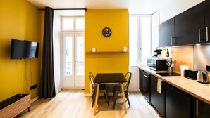 A compact kitchen with a dining area, a flat-screen TV mounted on the wall, and a clock on the wall. - Superb studio with balcony city center Opera (Lyon)
