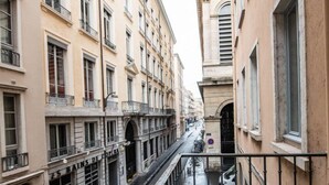 A narrow street with buildings on either side, a metal railing, and a yellow table in the foreground. - Superb studio with balcony city center Opera (Lyon)