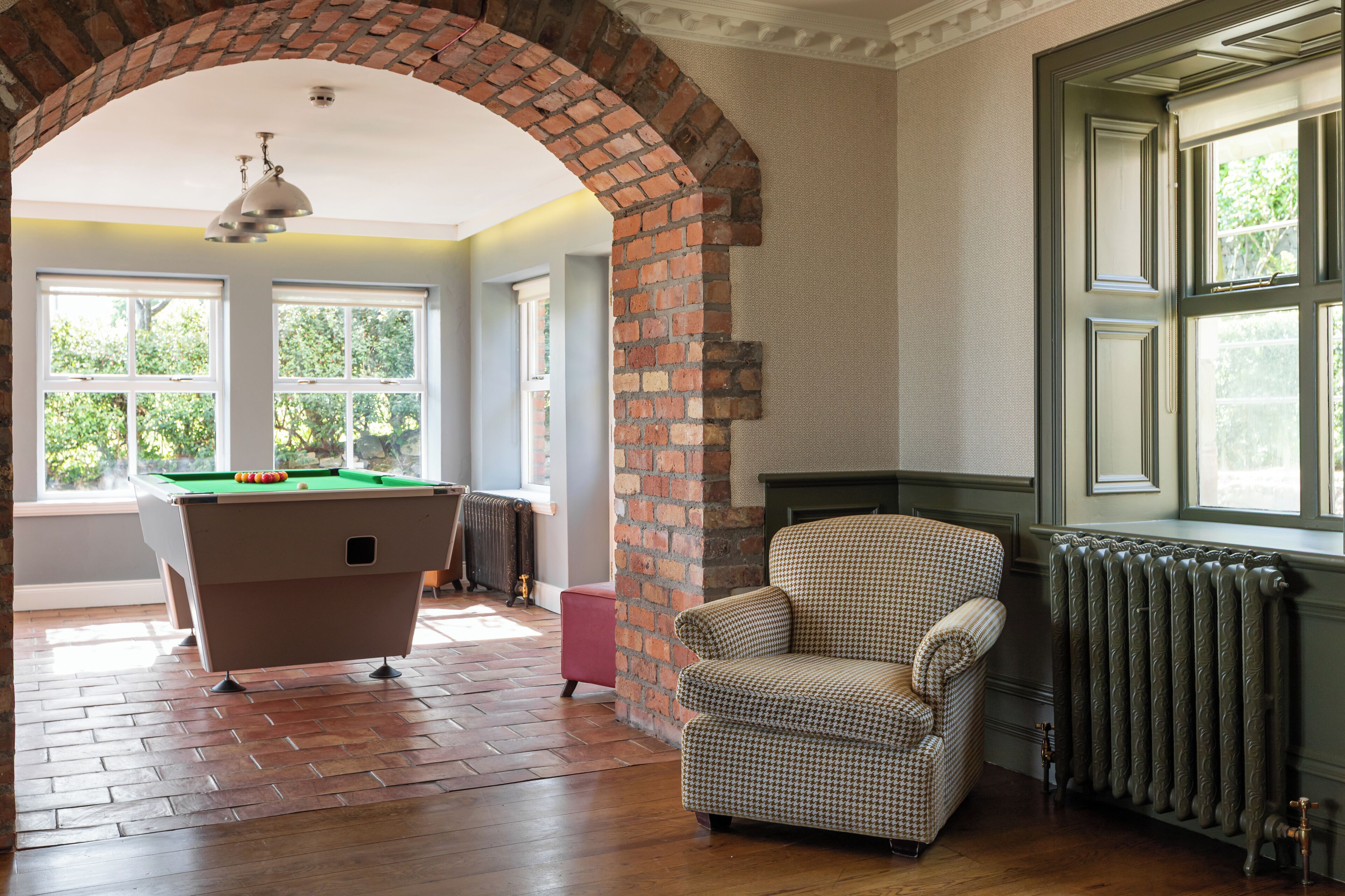 A room with a pool table, a checkered armchair, and a radiator near a window.
