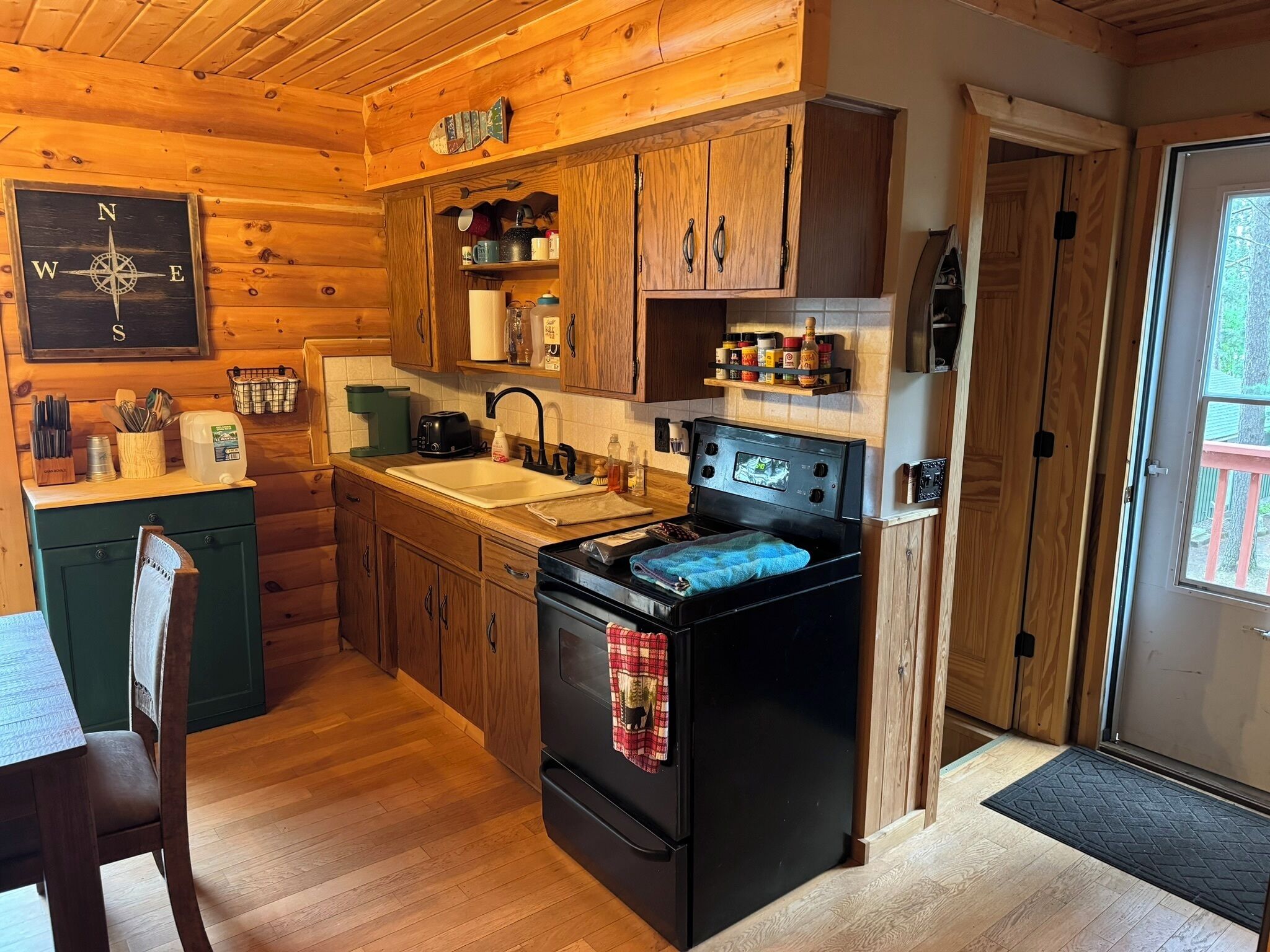 A cozy cabin-style kitchen with wooden cabinets, a black stove, and a window overlooking a deck.